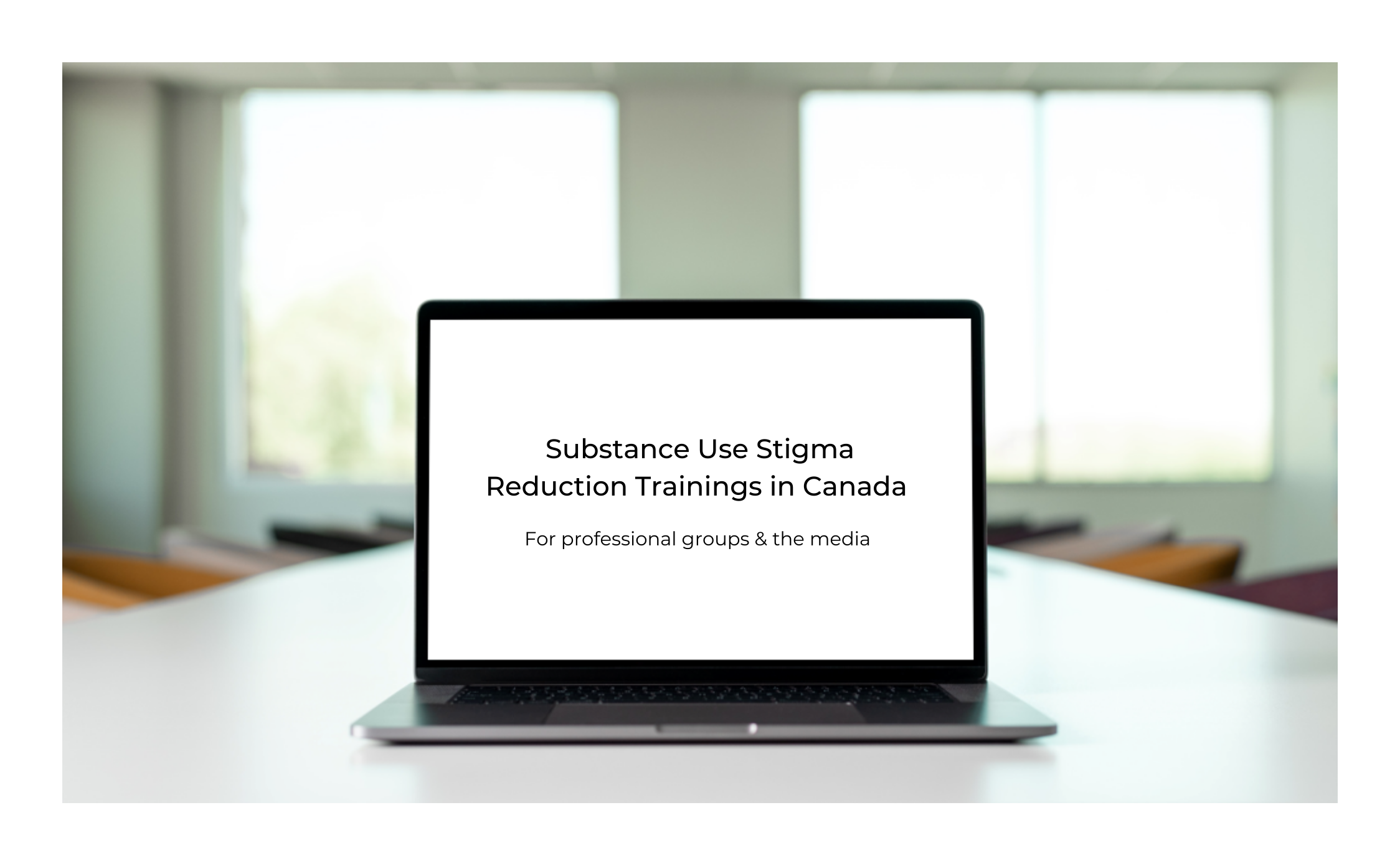 Open computer on a boardroom table. On the computer screen is written "Substance Use Stigma Reduction Trainings in Canada" in black text on a white background.